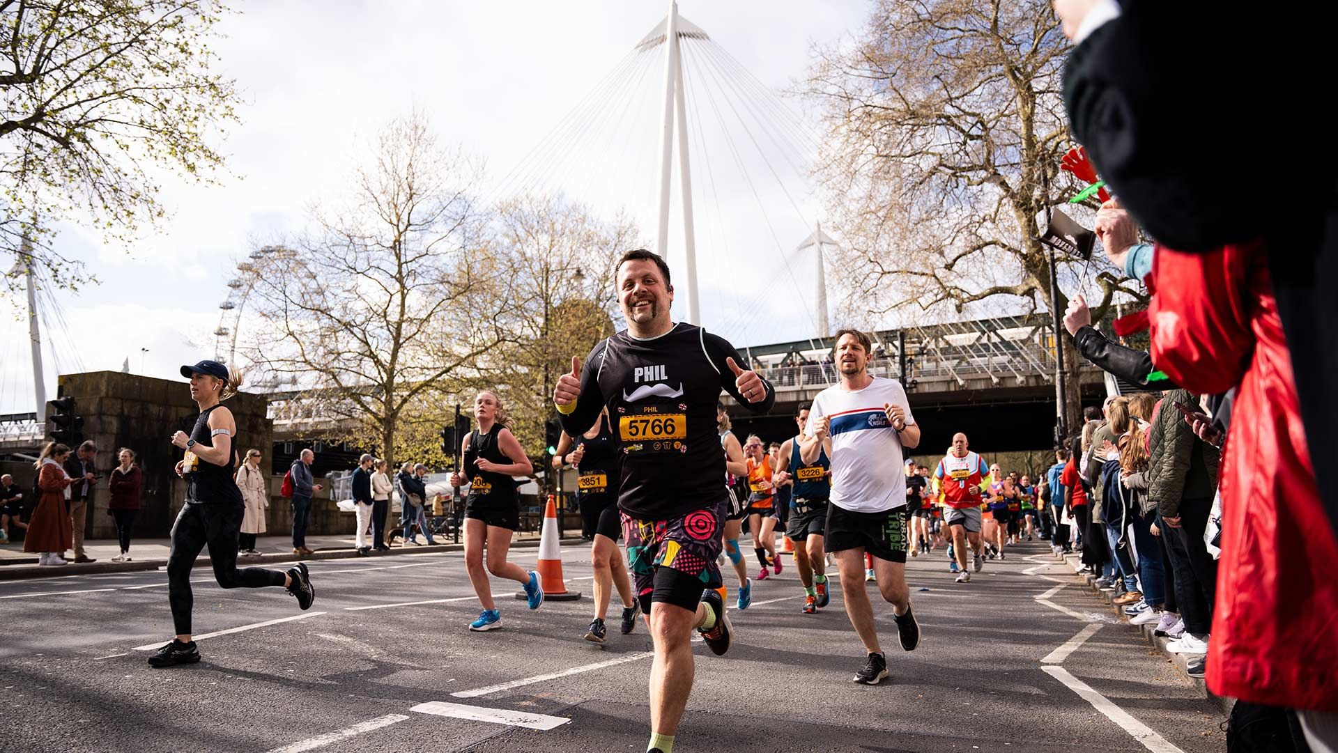 Photo of a man triumphantly running toward the camera with the London Eye visible in the background.