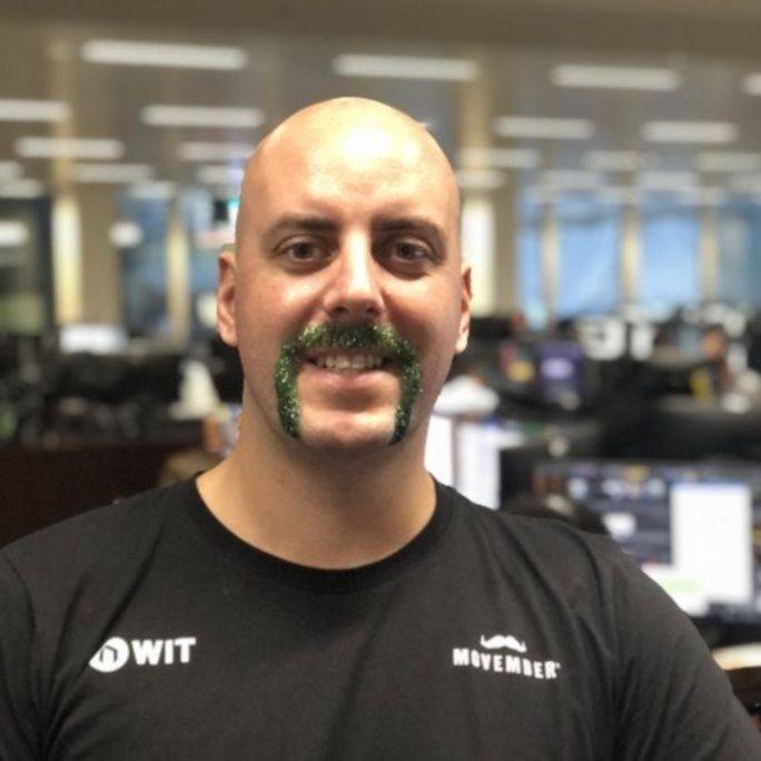 Photo of man, donning a superb, dyed green moustache, smiling to camera.