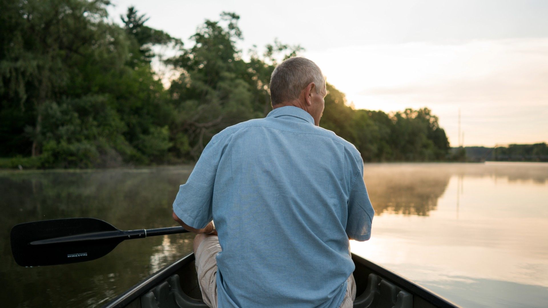 Elderly man on a canoe riding down a river as sun rises