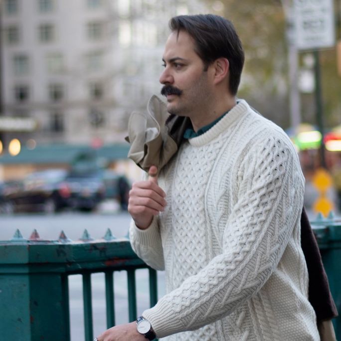 Photo of a man, seen from the side, wearing a stylish jumper and sporting a fine moustache.