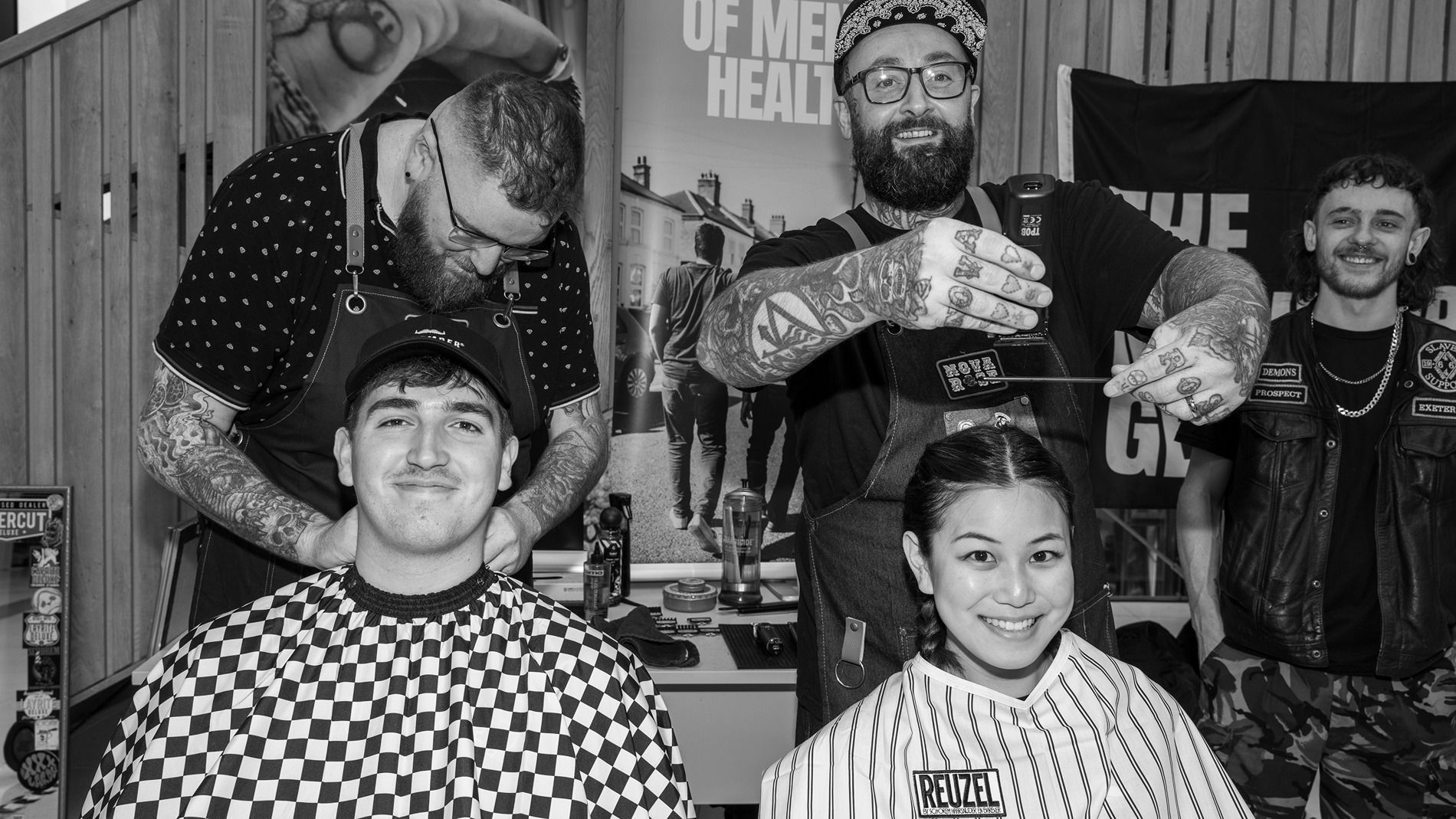 Two students sat in a chair getting a hair cut by Movember barbers