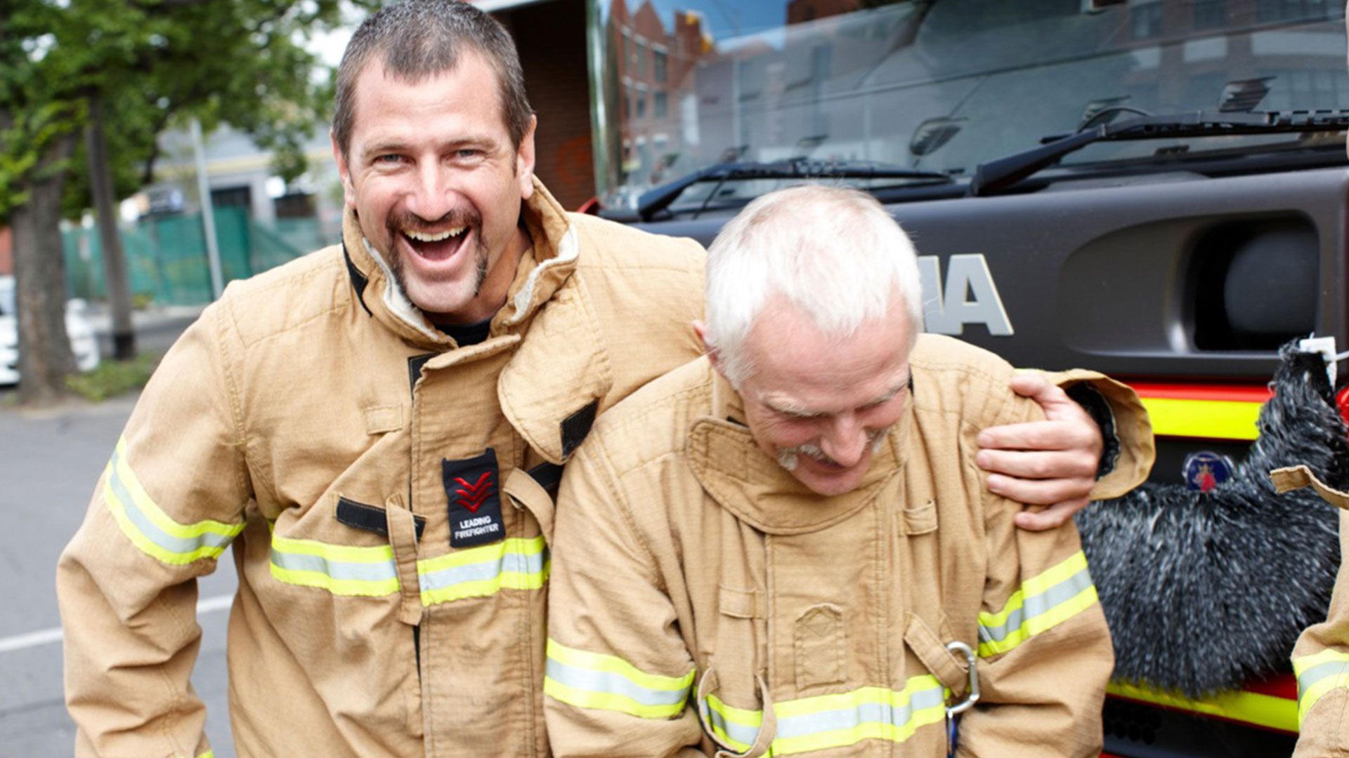 Two firefighters standing arm in arm and smiling