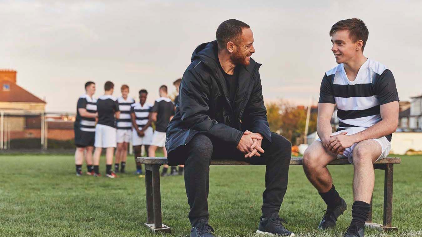 Rugby coach talking to young player about mental health.