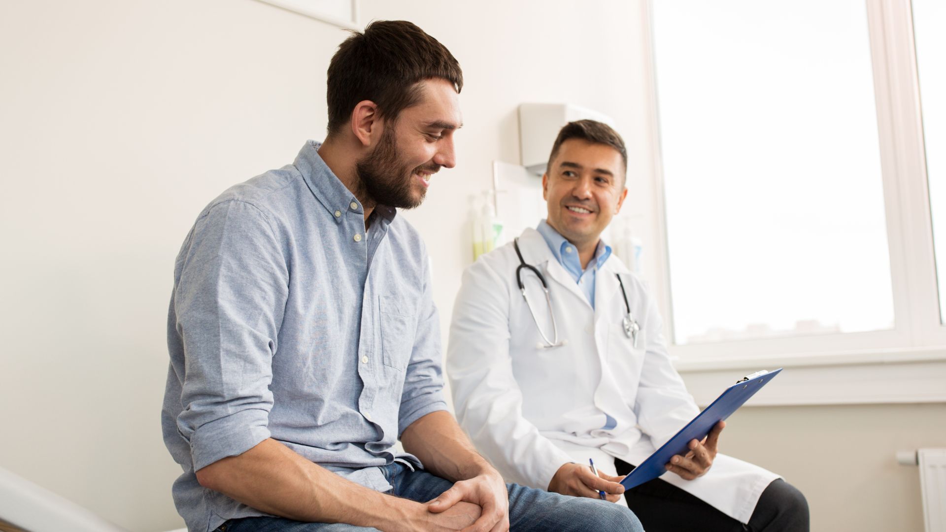 Male patient and doctor sitting down in doctor surgery having a conversation and smiling