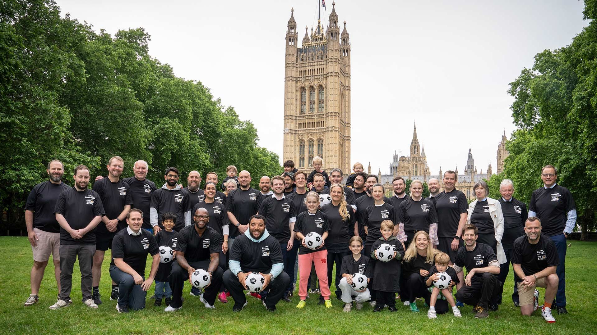 Photo showing fathers in Movember-branded shirts posing before Parliament.