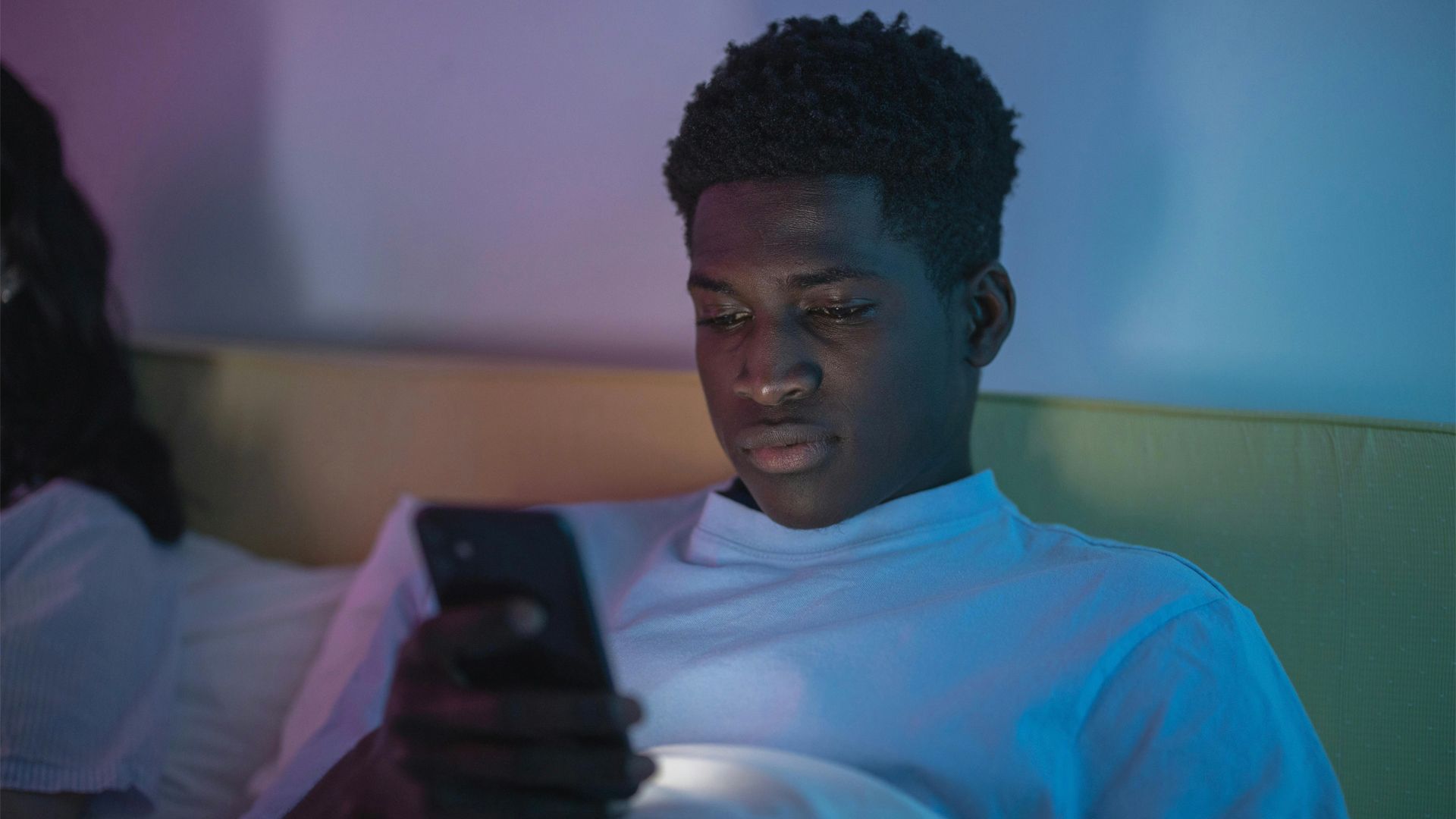 A young man views his smart phone, illuminated by its glow