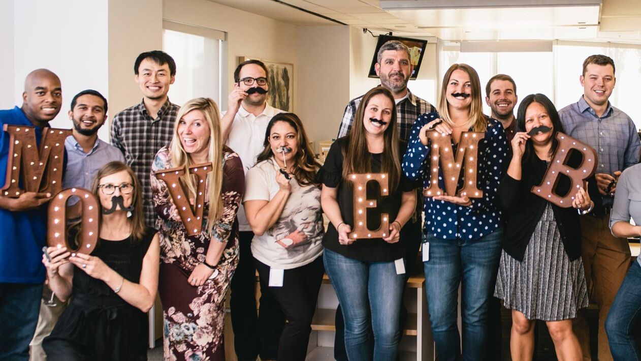 Group of people holding up letter spelling out Movember.