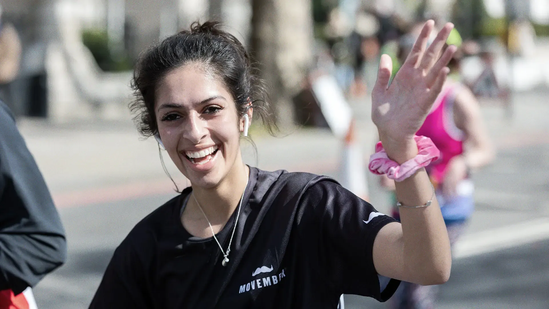 Athletic young woman participating in a marathon, smiling and waving to camera.