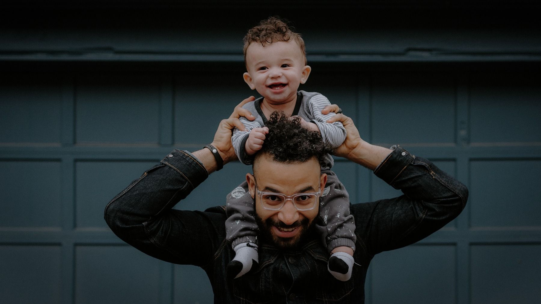 A baby sat on a fathers shoulders, smiling