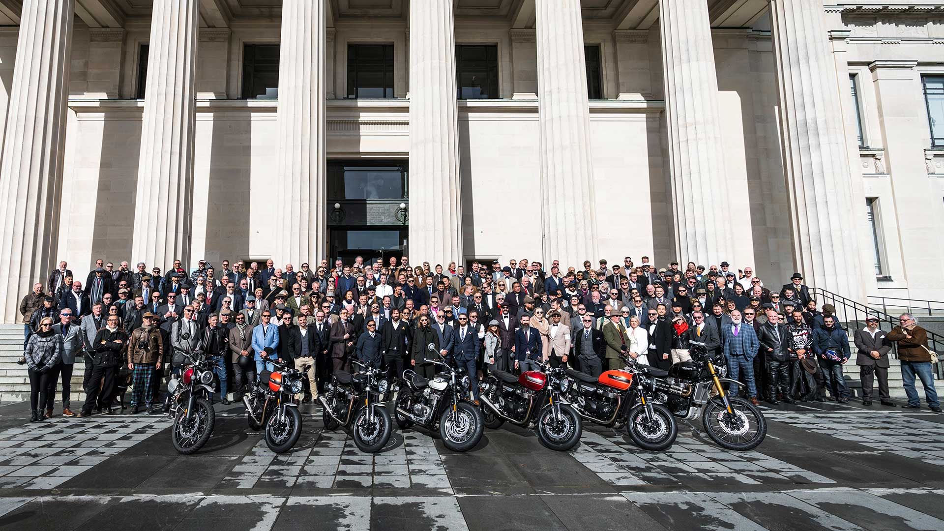 A large group of motorcyclists dressed in dapper attire, posing to camera.