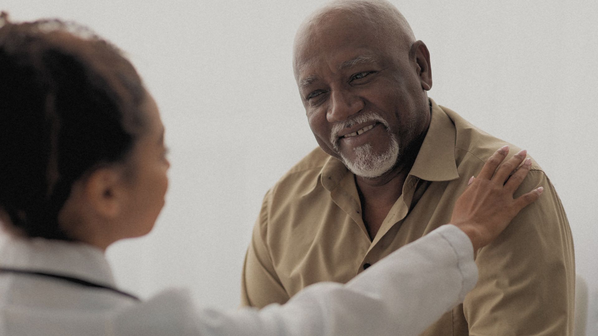 A doctor places her hand on her male patient's shoulder