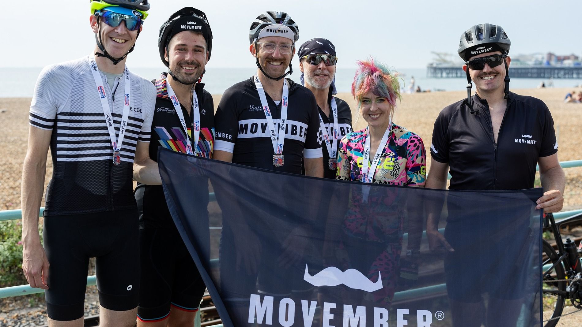 Photo of Movember supporter Stephen and his cycle team, holding a Movember banner at the finish line of the race in Brighton.