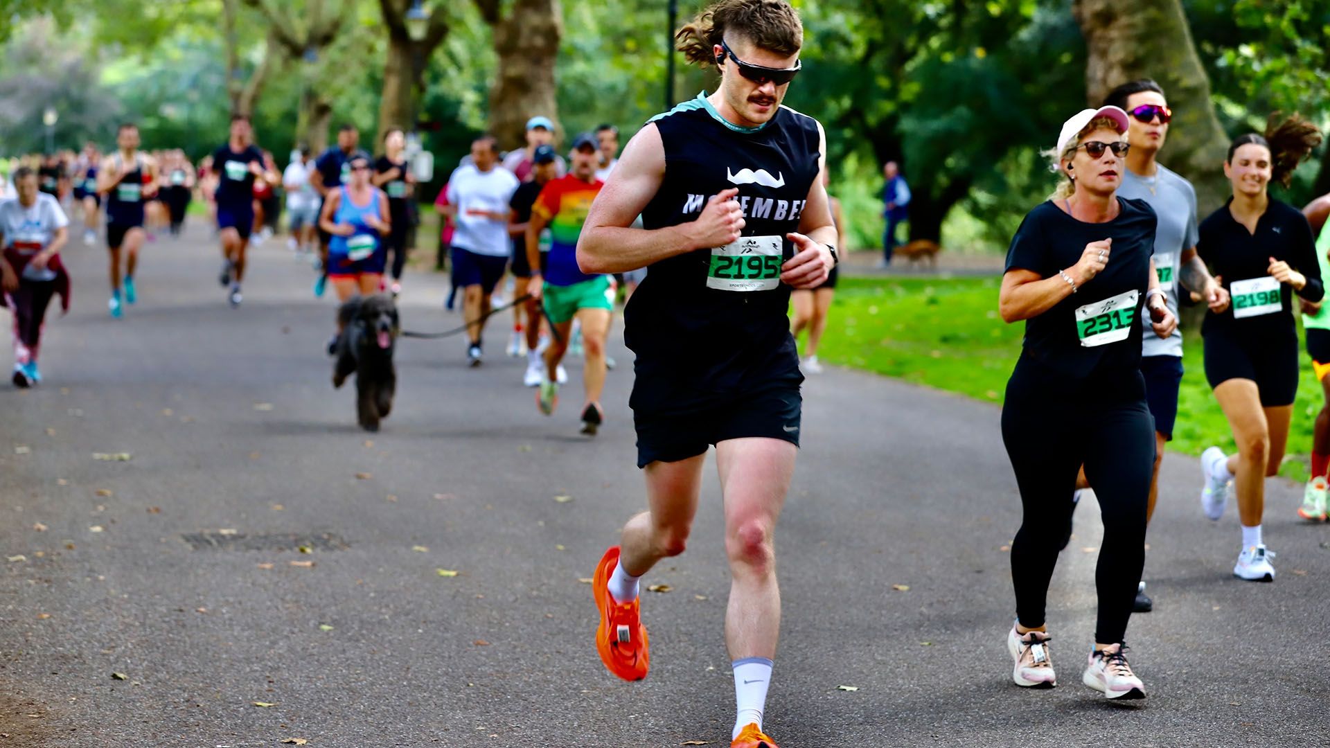 Photo of athletic man in Movember-branded running gear, powering toward camera in a public race.