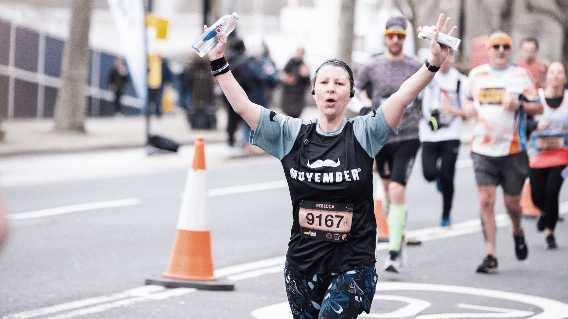 Photo of marathon runner in Movember-branded running gear, triumphantly lifting her arms to camera.