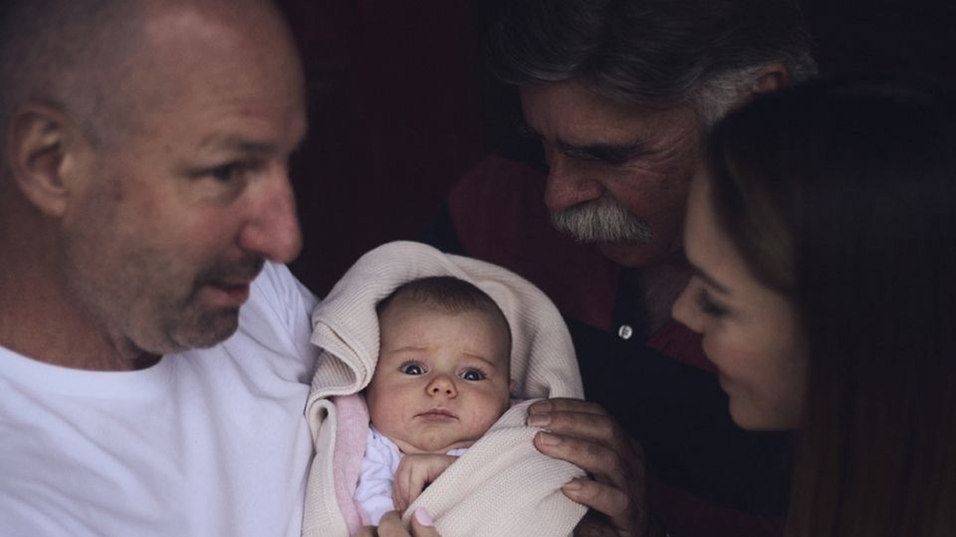 Photo of a father lovingly showing an infant to his family.