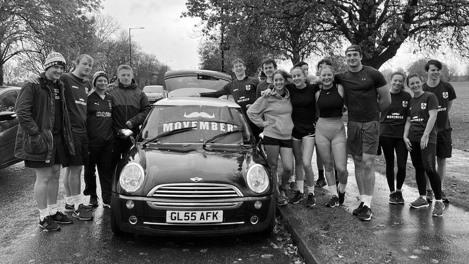 Group of people posing for camera wearing sports gear, on a road next to a mini car