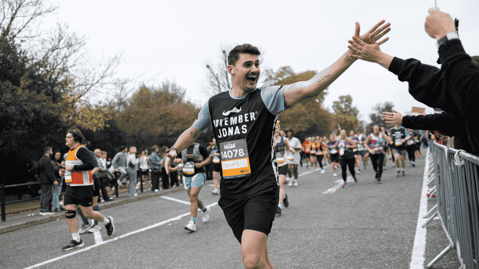 Photo of runner at a marathon wearing Movember-branded gear. The runner high-fives a spectator.