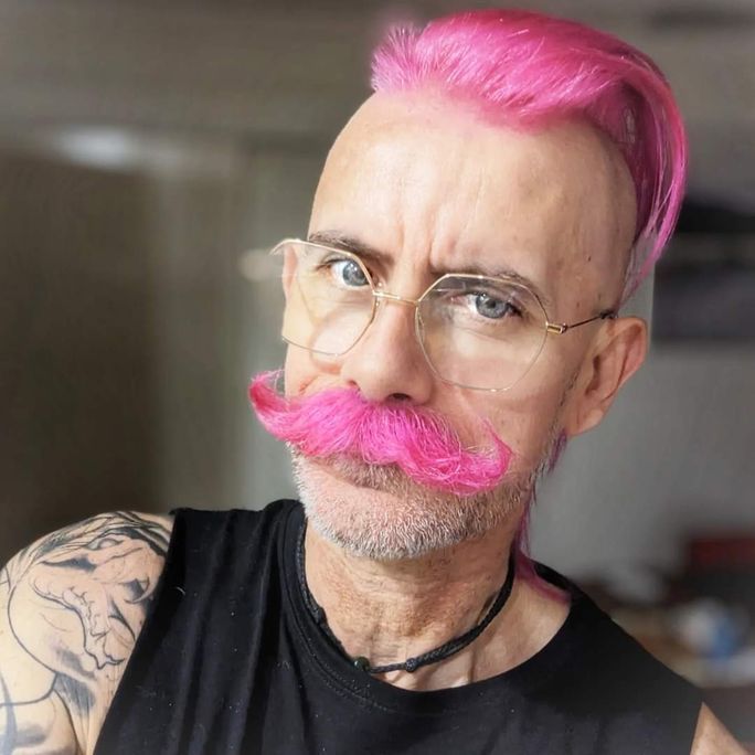 Photo of a man with a big and spectacular pink moustache, looking to camera.