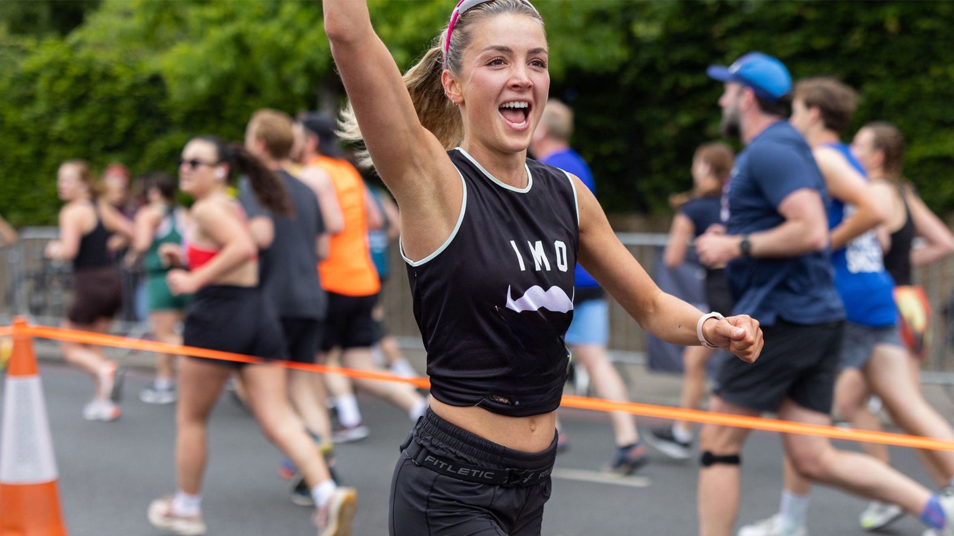 Athletic young woman participating in a marathon, smiling and waving to camera.