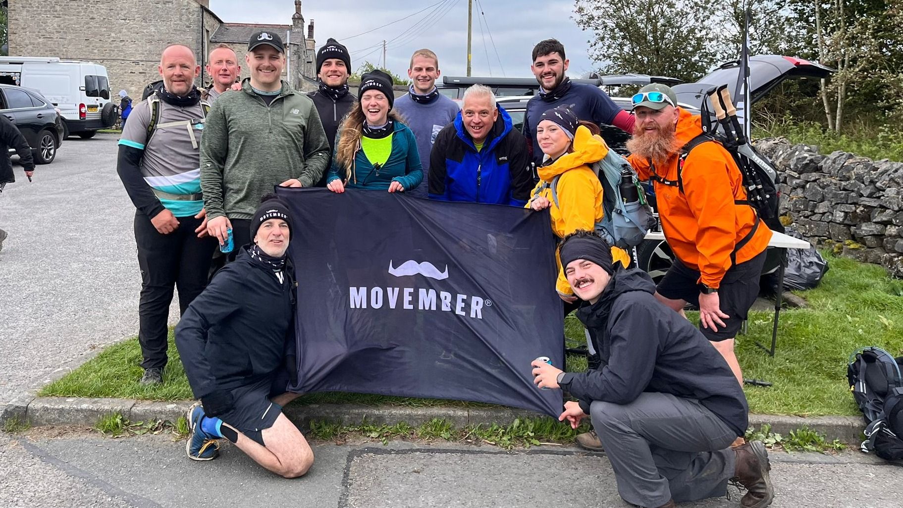 Group photo holding the Movember flag at the bottom of the Yorkshire Dales