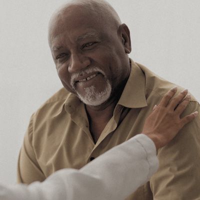 A photo of a person in a doctors coat resting their hand on the shoulder of an older male patient.