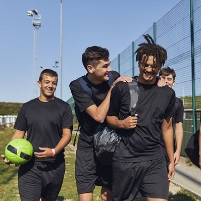 Four young men walking to football practice, laughing together.