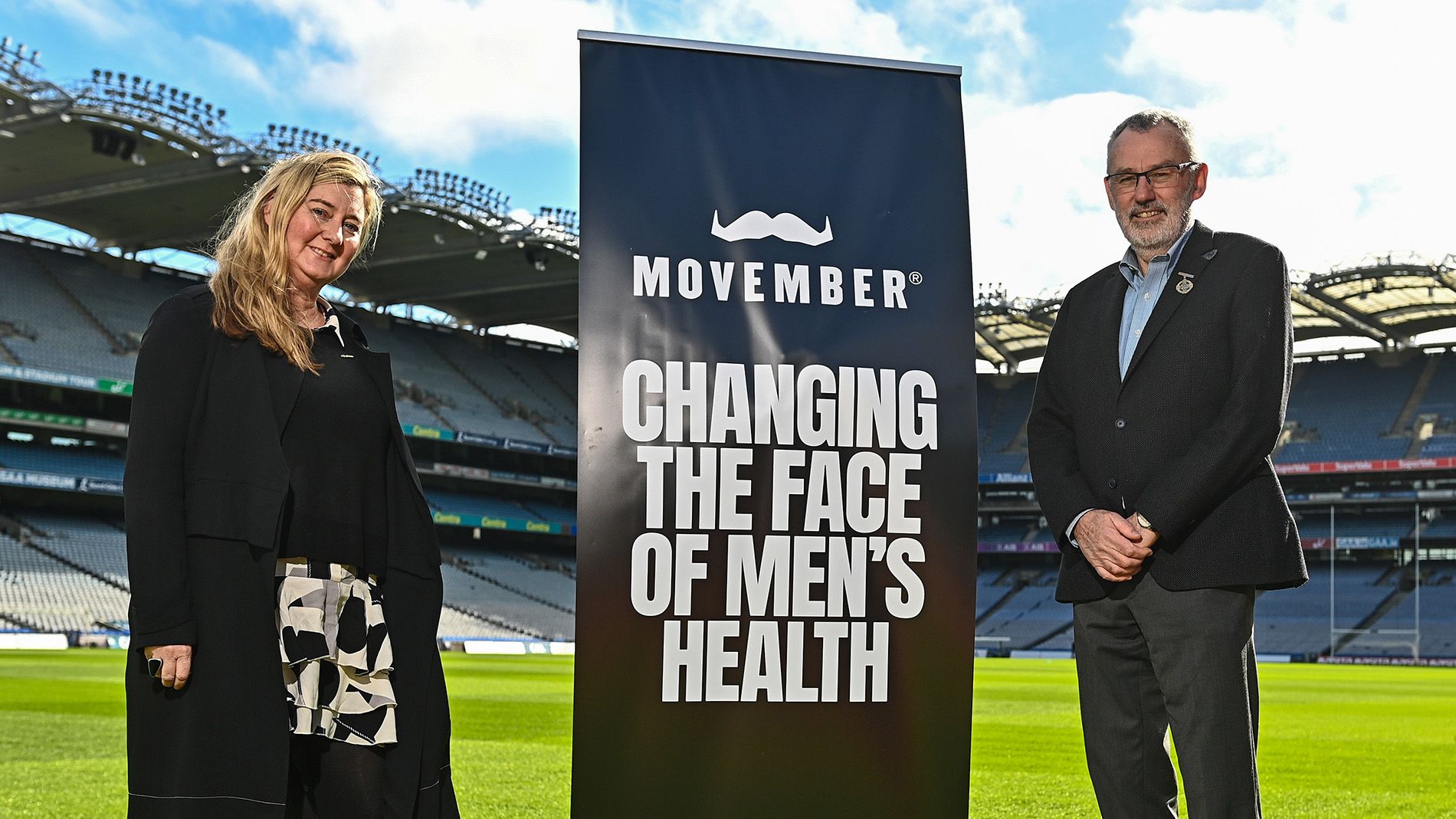 Movember staff lady and GAA staff man standing on Croke park football pitch posing for camera