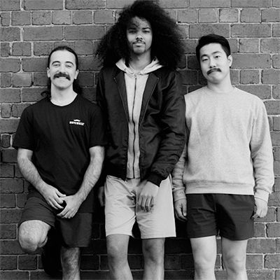 Black and white photo of three handsome young men, wearing glorious moustaches, smiling to camera.
