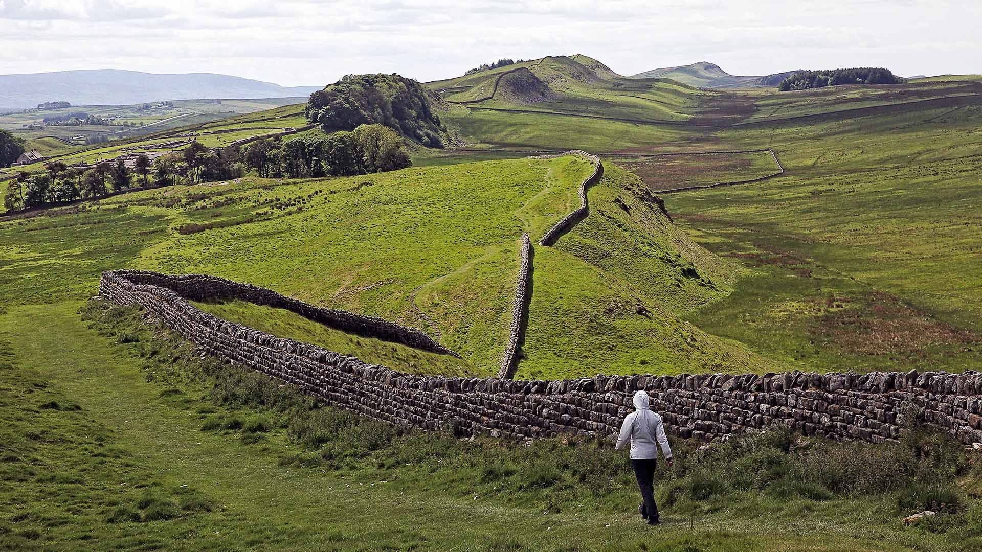 Sweeping, scenic view of solitary walker hiking past a hilly section of Hadrian's Wall.