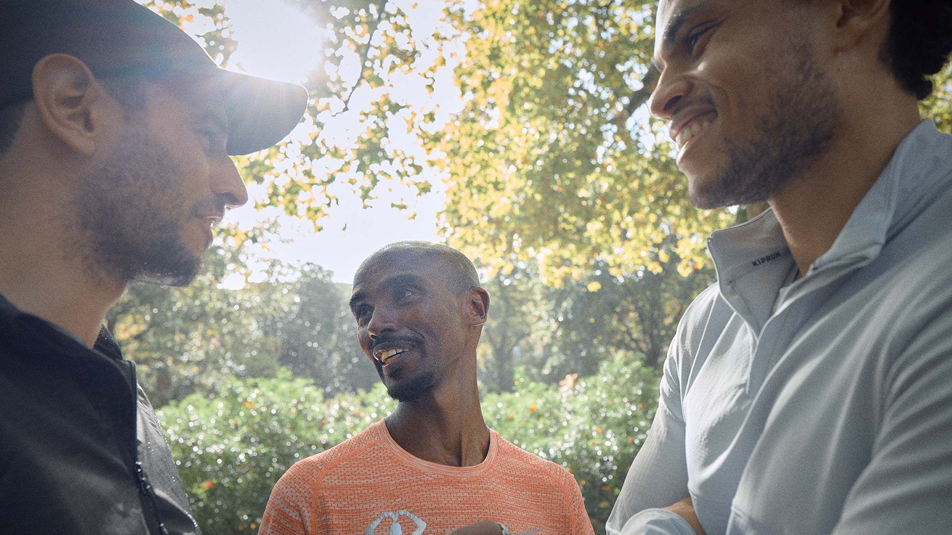 Photo of three men talking under some trees.