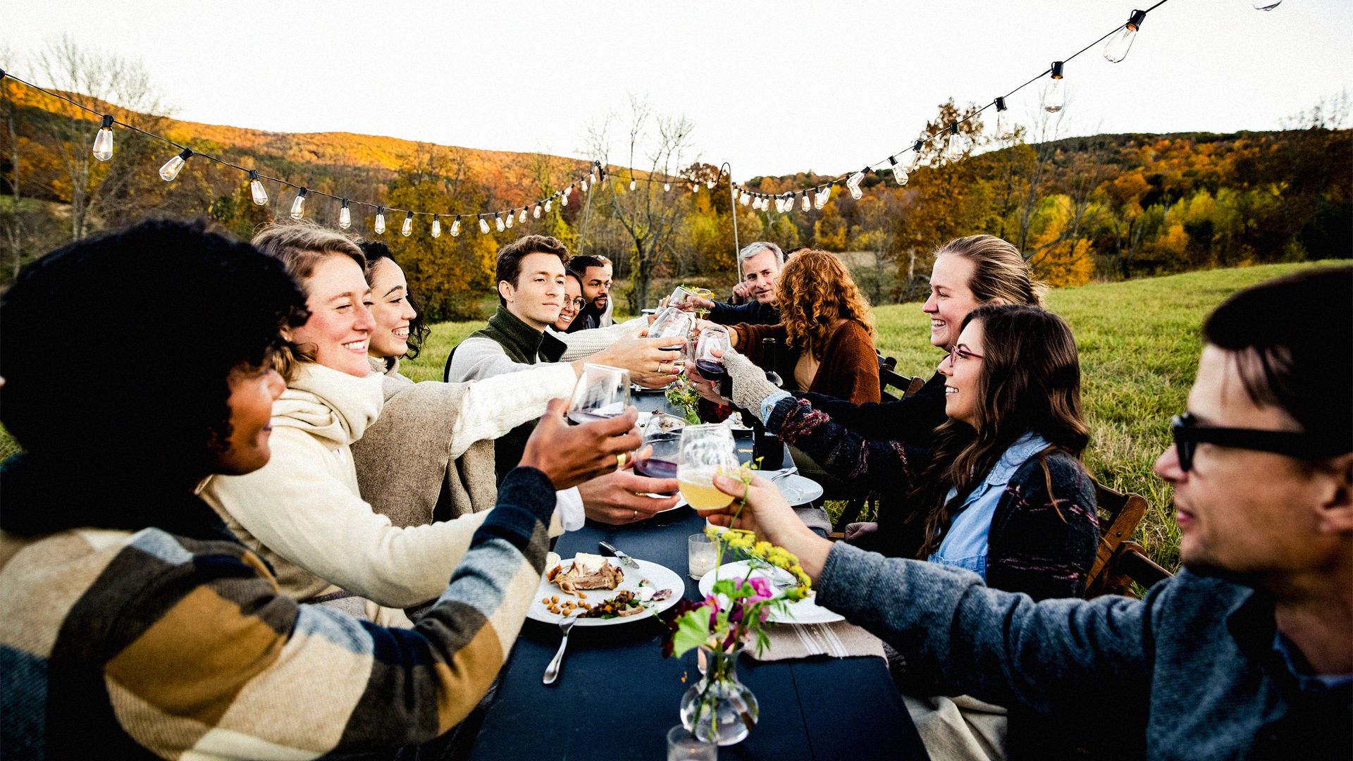 Photo of smiling people, enjoying an outdoor meal on a hillside.