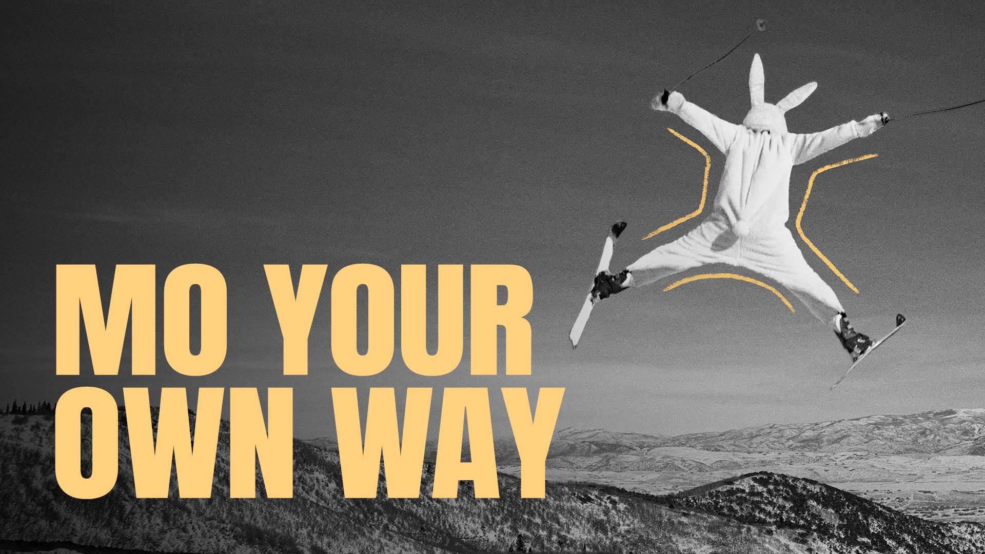 A black and white photo of a man jumping in skies while wearing a full rabbit suit. The words "MO YOUR OWN WAY" are superimposed.