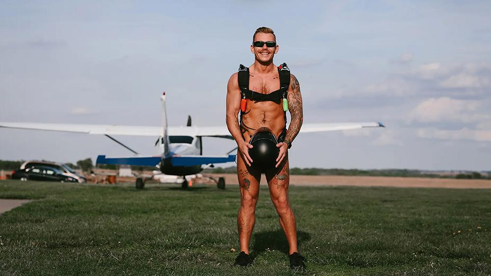 Naked man skydiver standing on airfield, ready to raise money for men's health.