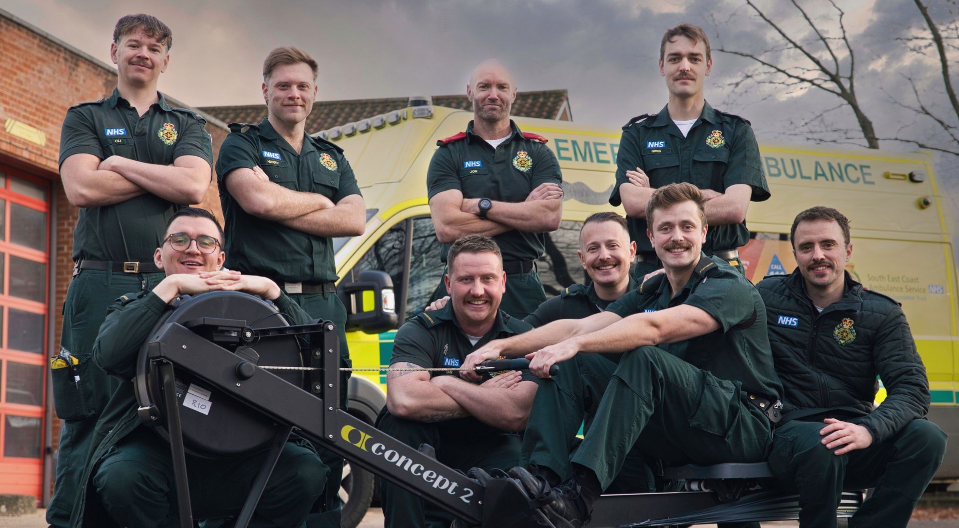 Ambulance service team standing around a rowing machine with an ambulance in the background