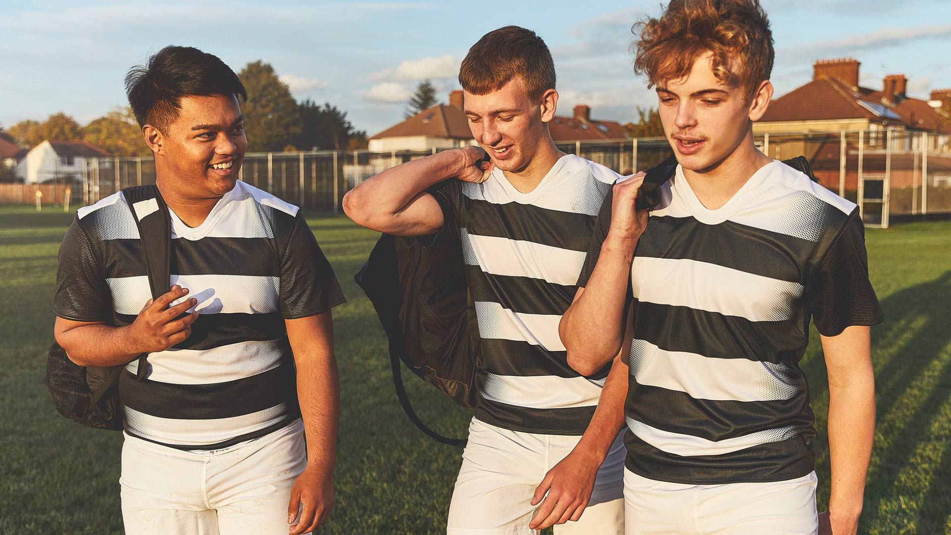 Young men in striped rugby sport attire chatting on a field after a game.